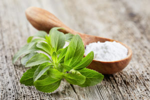 Foglie di stevia accanto a un cucchiaino di dolcificante in polvere o cristalli