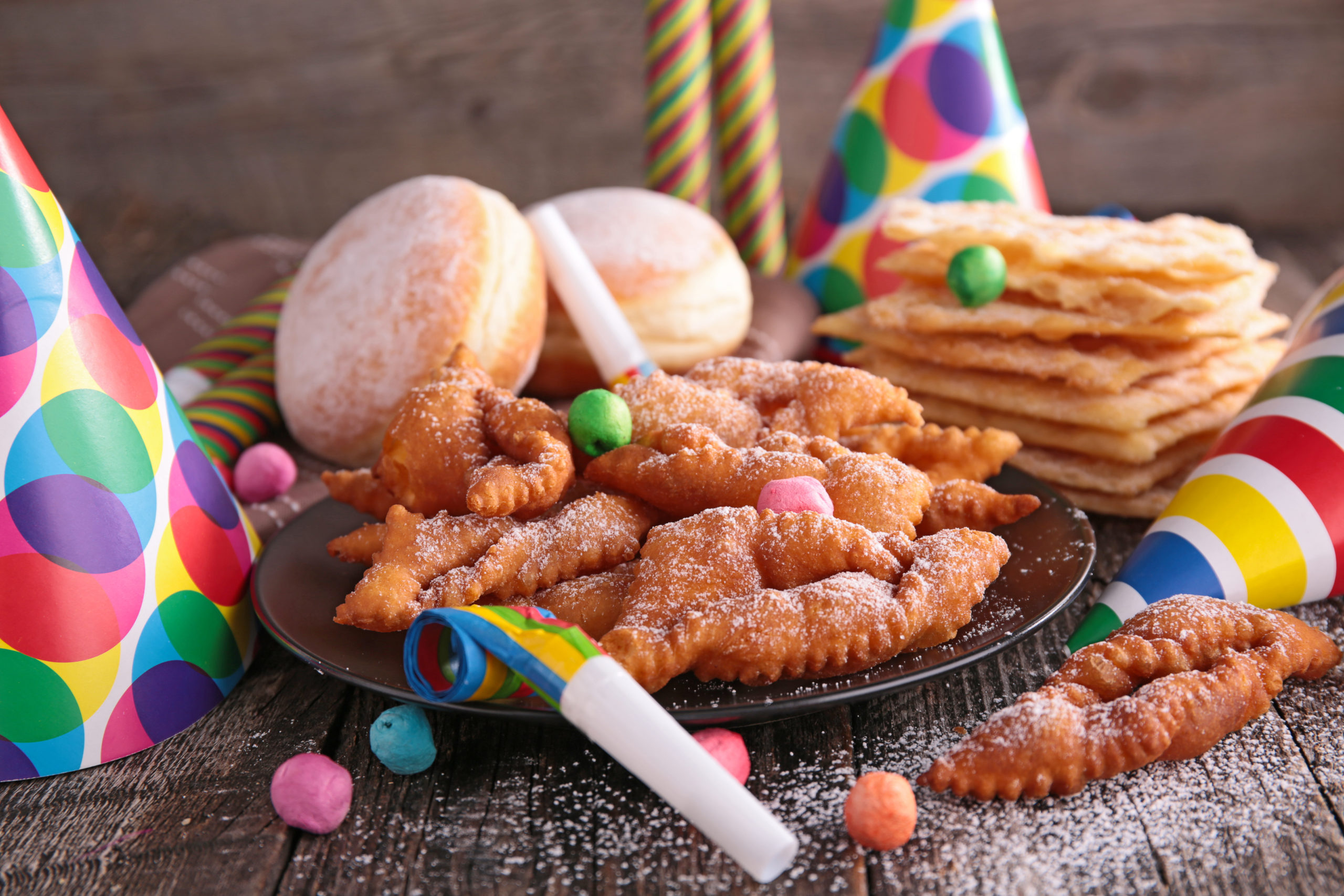 Chiacchiere, bugie o frappe, con bomboloni o krapfen e caramelle, con trombetta e cappellini di Carnevale
