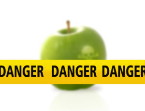 Un nastro giallo con la scritta danger davanti a una mela verde; concept: sicurezzaalimentare, allerta alimentare, allerte alimentari