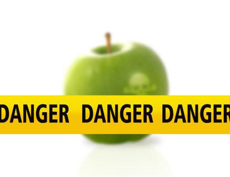Un nastro giallo con la scritta danger davanti a una mela verde; concept: sicurezzaalimentare, allerta alimentare, allerte alimentari