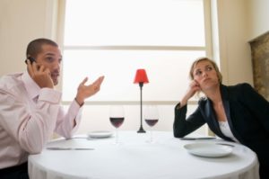 Due persone al tavolo di un ristorante: l'uomo parla al telefono, la donna si annoia