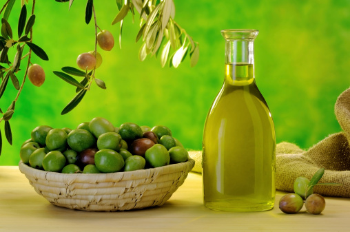 Bottiglia di olio extravergine accanto a cesto di olive