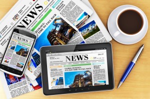 Giornale cartaceo e giornale online su smartphone e tablet accanto a penna e caffé; concept: giornalismo, finti articoli