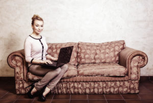 Donna seduta sul divano con un computer portatile sulle gambe; concept: ecommerce, frodi online, truffe, antitrust