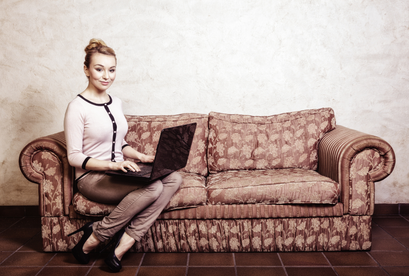 Donna seduta sul divano con un computer portatile sulle gambe; concept: ecommerce, frodi online, truffe, antitrust