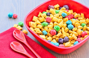 Ciotola di cereali da colazione colorati su un tavolo accanto a tovagliolo e due cucchiai; concept: Kellogg's