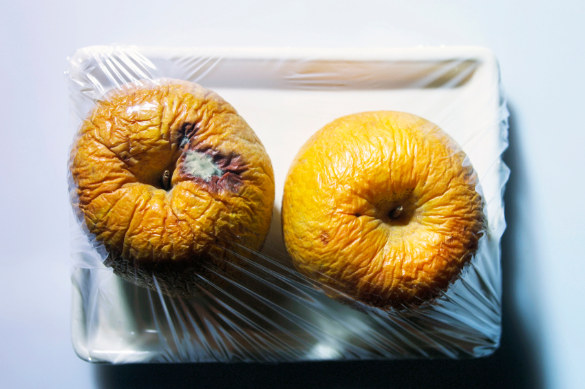 Mele troppo mature in una vaschetta di plastica con pellicola; concept: muffa, mele marce