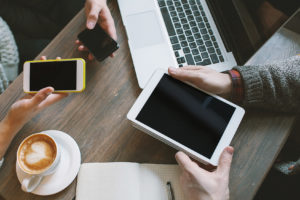 Hands with smartphones, tablet over table with laptop and coffee app
