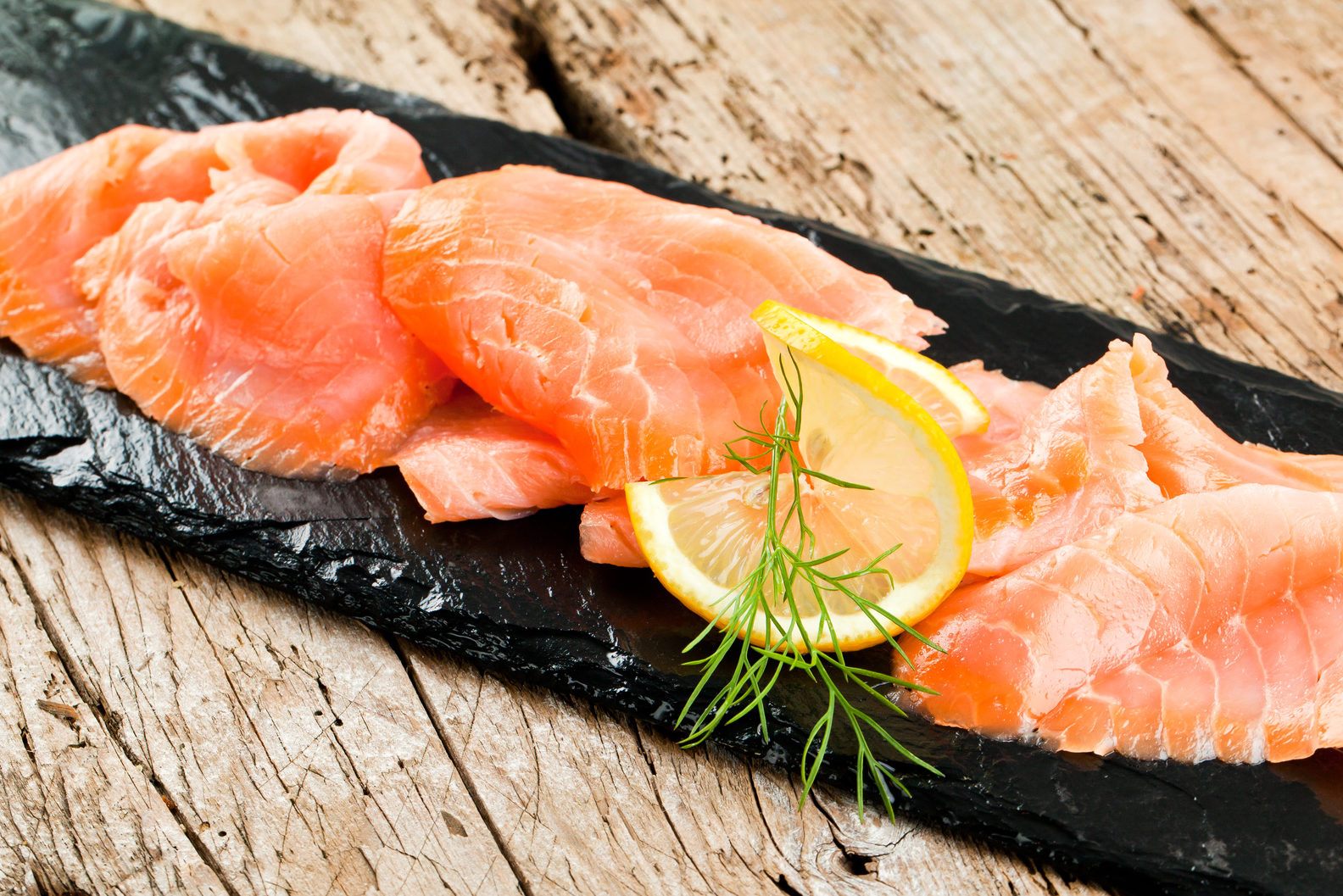 fette di salmone affumicato con limone e aneto su un vassoio di ardesia