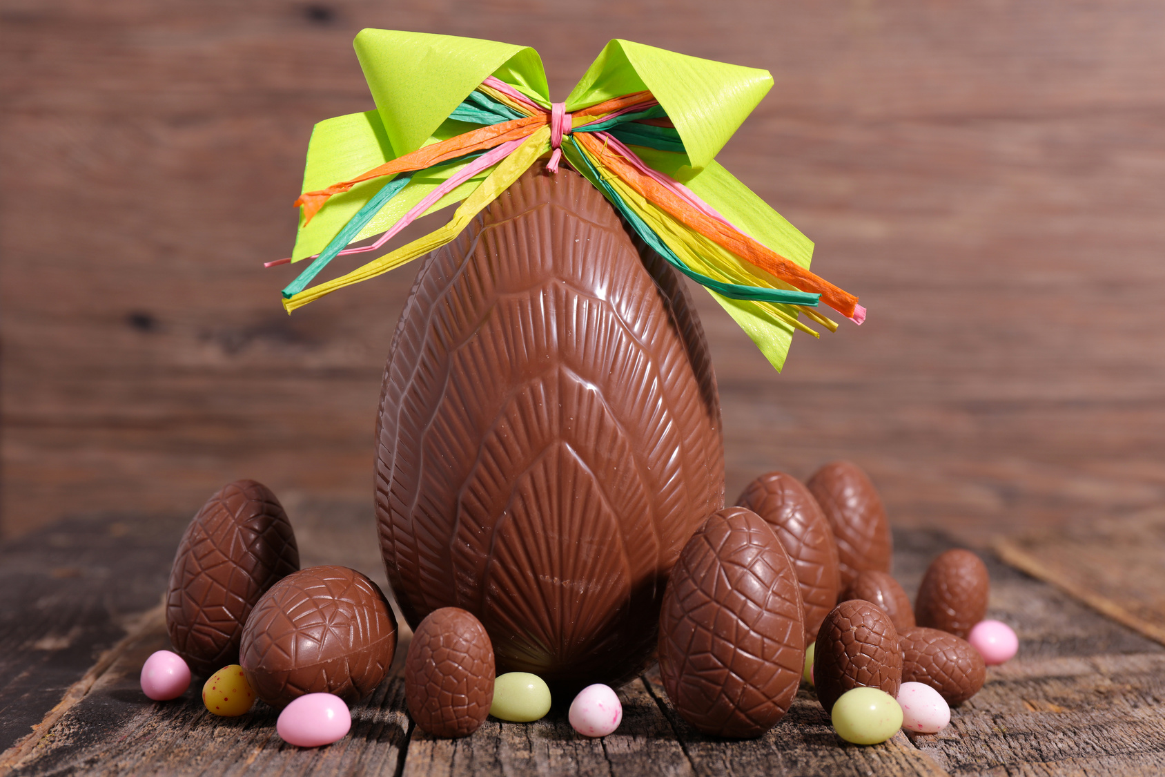 Uovo di Pasqua di cioccolato con fiocco, circondato da uova di cioccolato più piccole e confetti