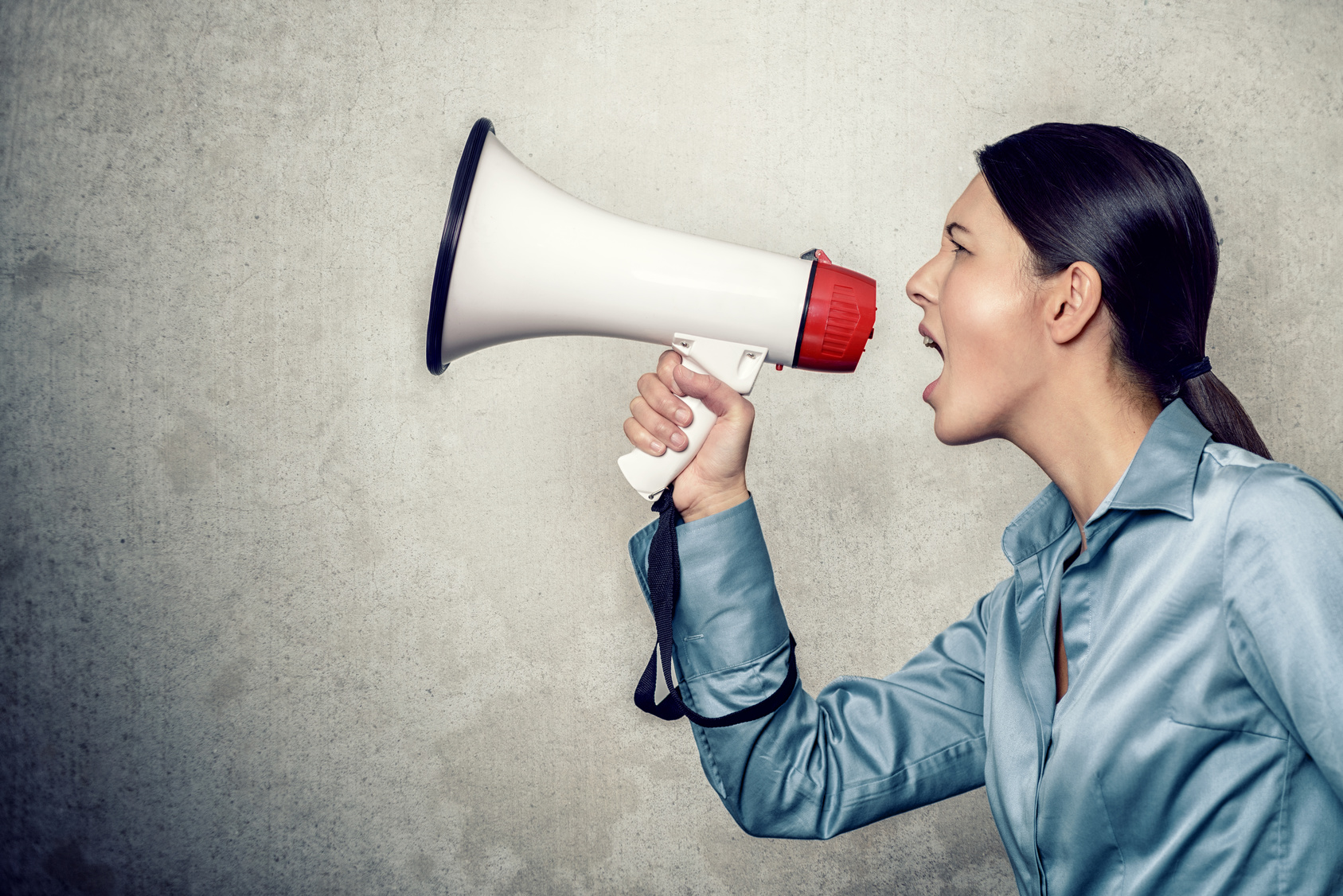 Giovane donna urla in un megafono; concept: allerta, ritiro, richiamo, rischio alimentare