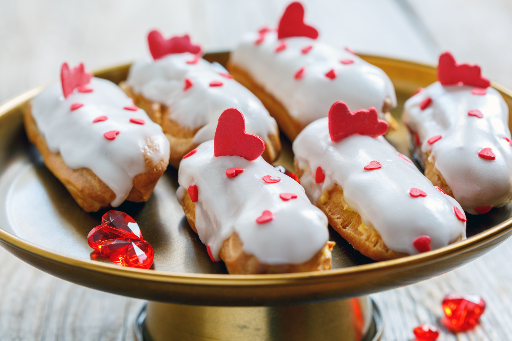 Eclairs con glassa bianca alla vaniglia e cuoricini di zucchero su un'alzatina