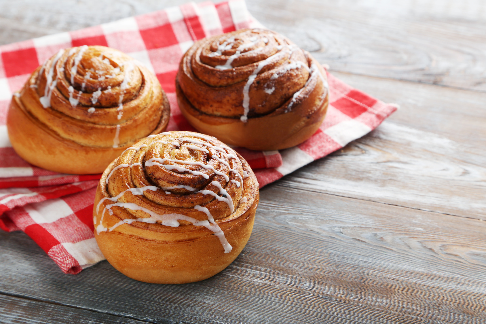 Cinnamon rolls con glassa su un tovagliolo a quadretti; concept: brioche, merendine