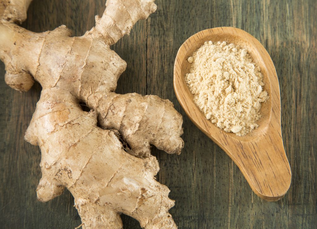Radice di zenzero accanto a un cucchiaio di legno con zenzero in polvere