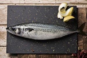 Uno sgombro su un tagliere di ardesia con fette di limone; concept: pesce azzurro