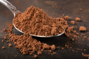 Cucchiaino pieno di cacao in polvere su sfondo scuro