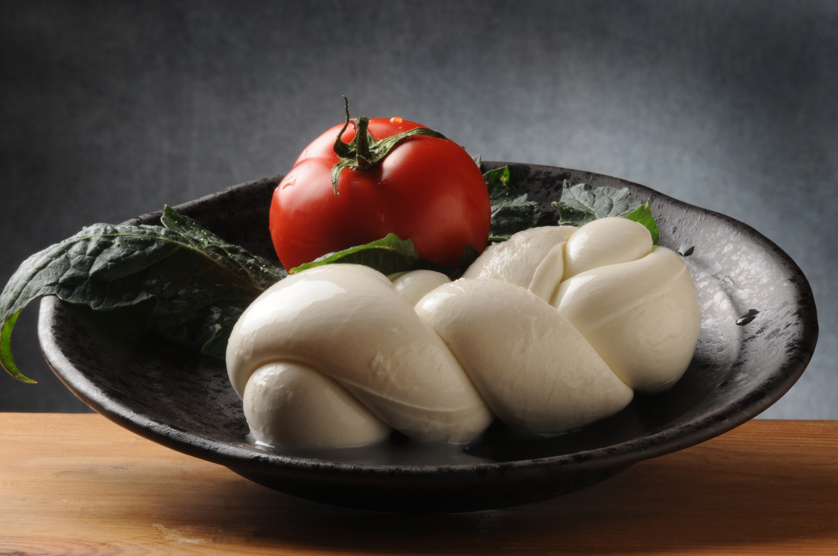 Treccia di mozzarella in un piatto nero con pomodoro