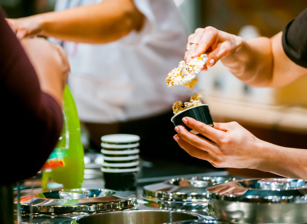 Gelataio prepara una coppetta di gelato in gelateria sopra i pozzetti dei gelati