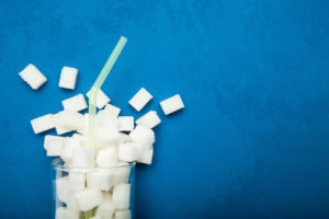 Spilled sugar from a glass on a blue background. Giant sugar concentration in everyday beverages.