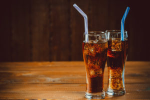 Beautiful cold drink of Cola with ice cubes with a boiler straws in glasses on wooden background with free space