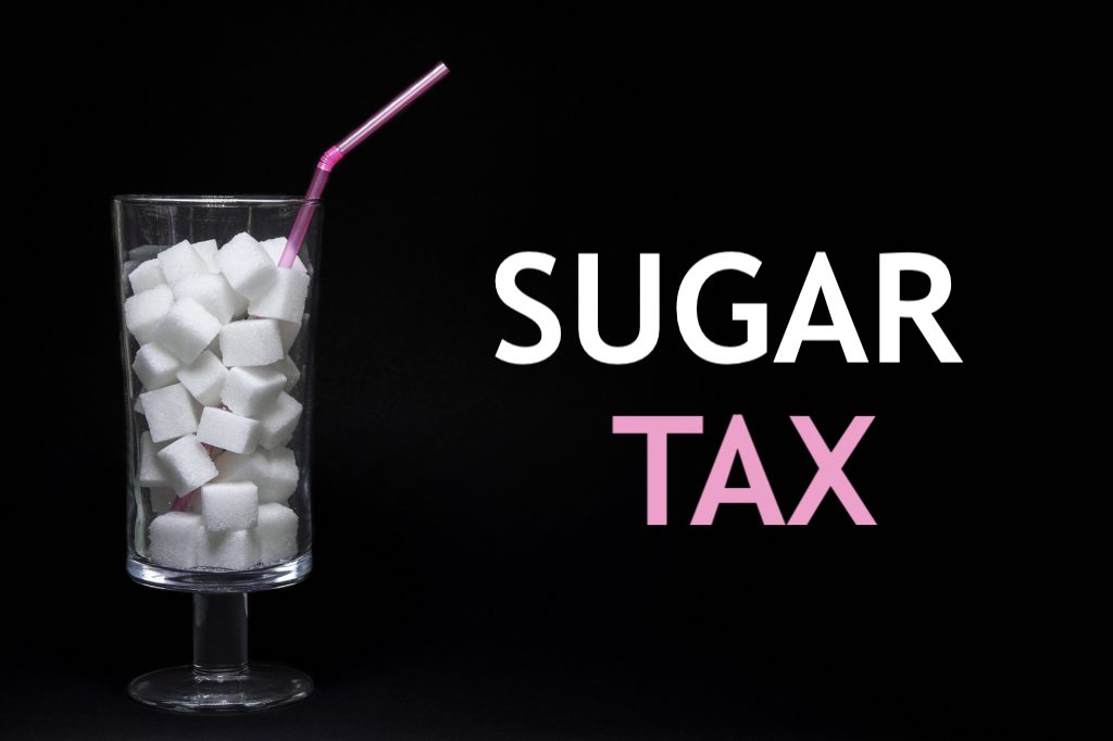 Bicchiere con cannuccia pieno di cubetti di zucchero cibo la scritta sugar tax; concept: bevande zuccherate