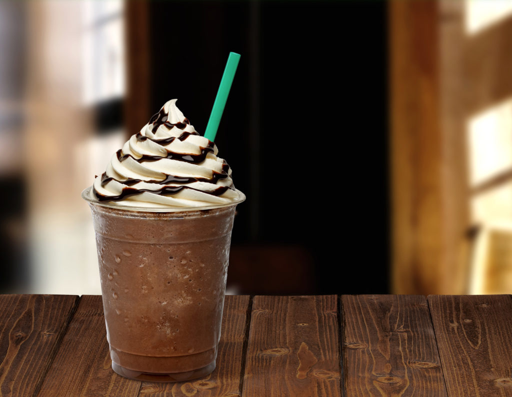 Frappuccino in takeaway cup on wooden table isolated on cafe background