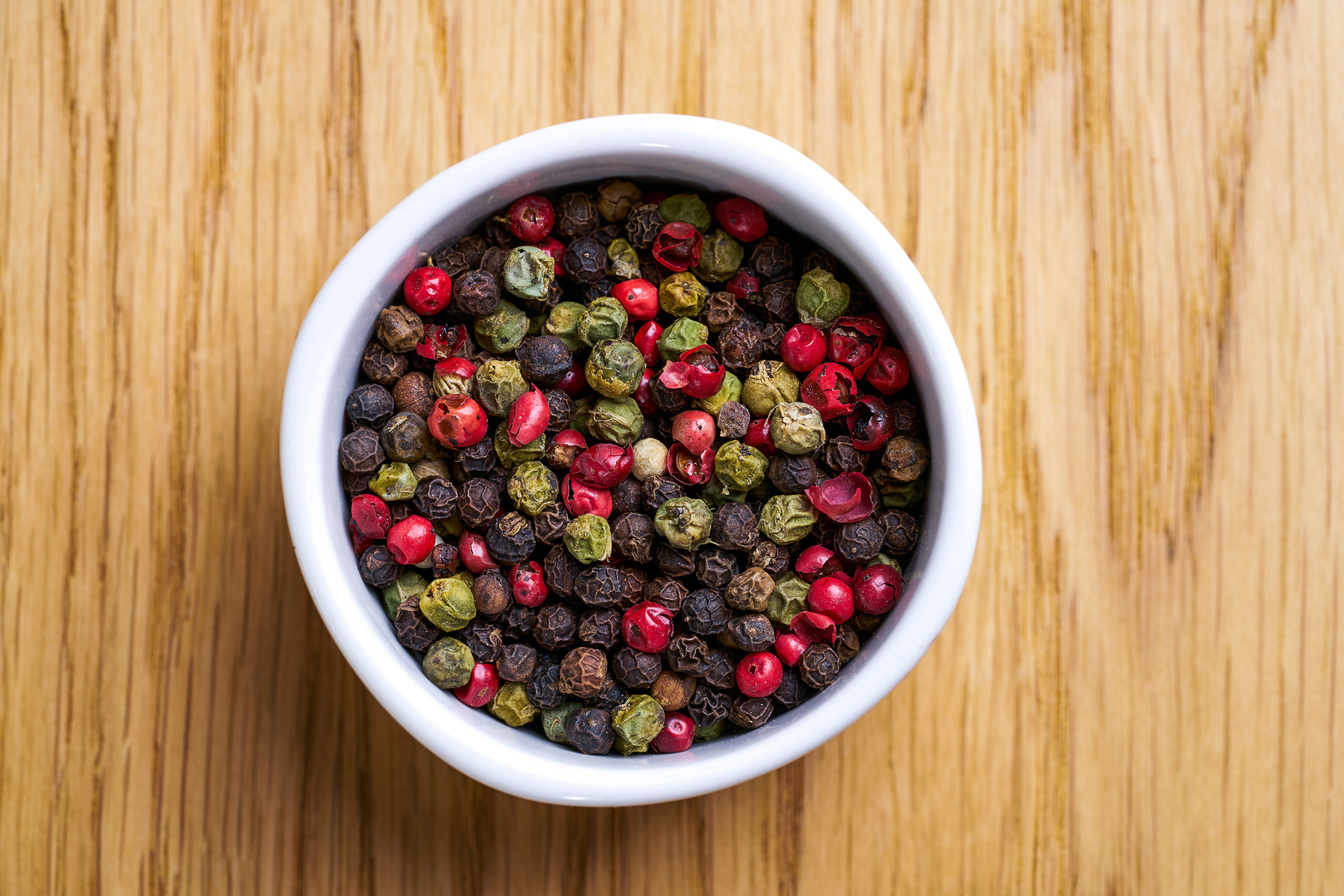 White bowl with pepper mix. Various pepper served in white bowl on wooden background.