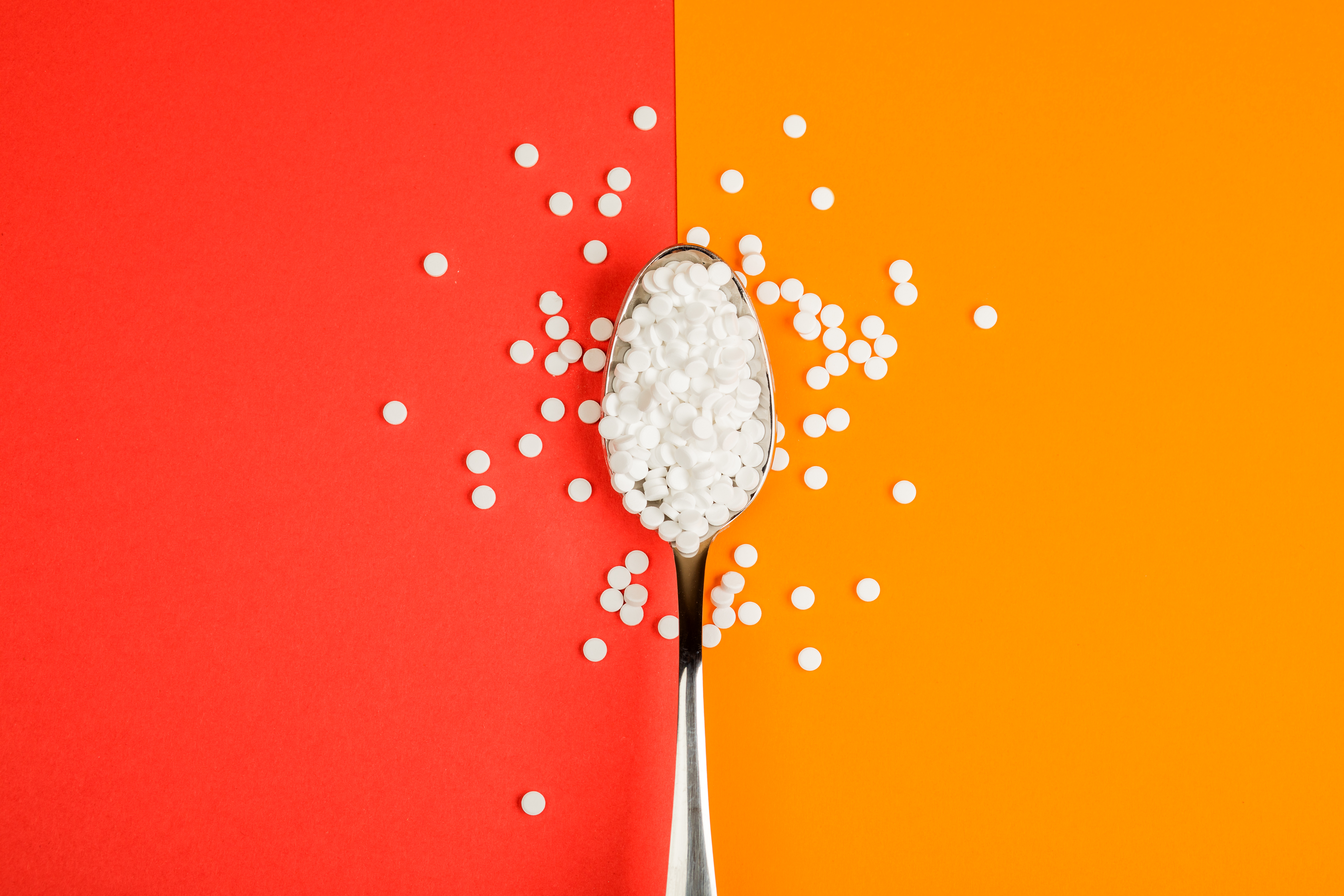 Cucchiaio per pastiglie per la sostituzione dello zucchero su sfondo arancione e rosso dolcificanti sucralosio edulcoranti zucchero dolce