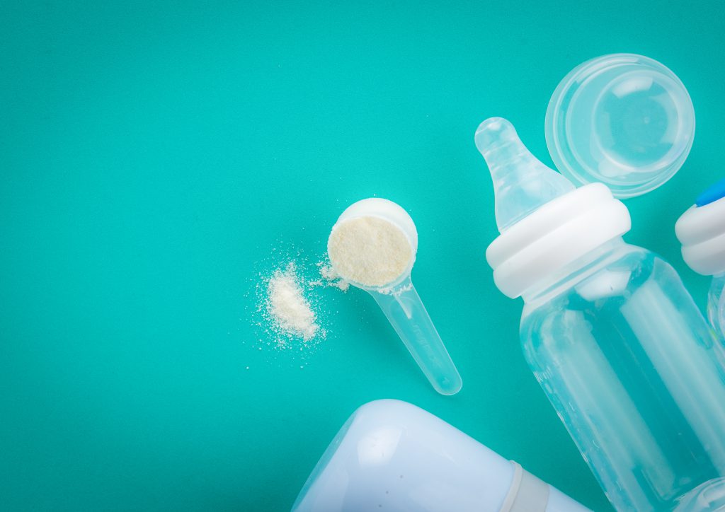 Misurino di latte in polvere, con biberon trasparente su sfondo verde-azzurro sicurezza alimentare