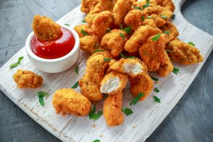 Nuggets di pollo panati e fritti su un tagliere di legno con ciotola di ketchup