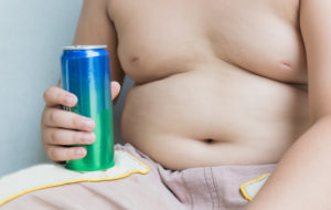 Bambino sovrappeso a torso nudo con lattina di bevanda zuccherata in mano; concept: alimentazione, obesità, bambini, cattive abitudini, sugar tax