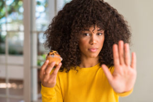 Ragazza con in mano un dolce muffin al cioccolato, che fa segno di fermarsi con l'altra mano. Stop allo zucchero, anche per carboidrati