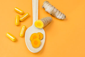 Radici di curcuma intere e affettate, fette di curcuma su un cucchiaio e capsule di curcuma