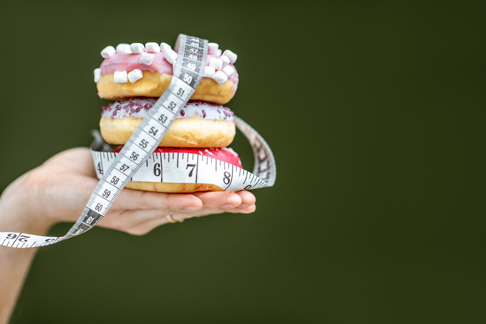 Sweet donuts with measurement tape on the green background