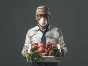 Uomo d'affari con maschera protettiva che tiene in mano una cassa con verdure inquinate e velenose, concetto di inquinamento alimentare residui di pesticidi