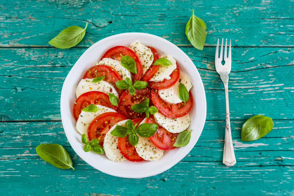 Delicious caprese salad with ripe tomatoes and mozzarella cheese with fresh basil leaves. Italian food.