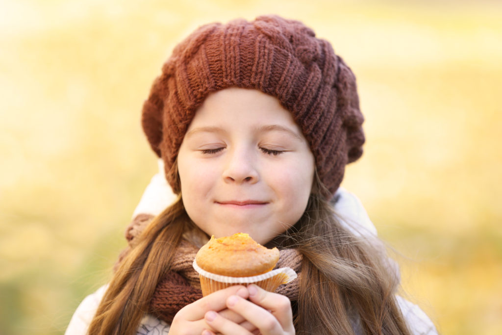Bambina con cappello di lana annusa un muffin prima di mangiarlo