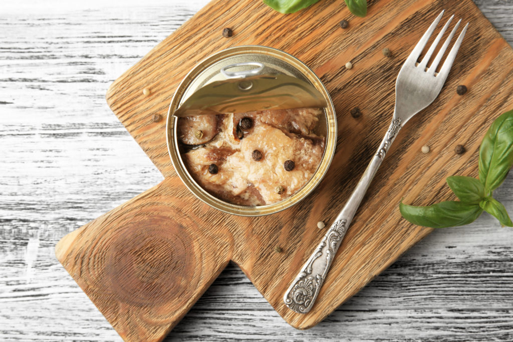 Open tin can with fish on wooden board