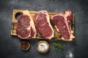 Fette di carne rossa su un tagliere di legno accanto a ciotoline di sale, pepe e erbe aromatiche