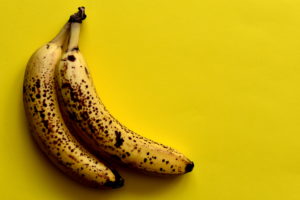 Due banane mature con macchie marroni sul tavolo giallo brillante, vista dall'alto, spazio vuoto.