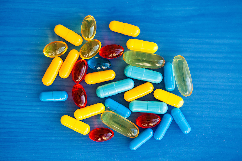 Capsule e capsule molli gialle, rosse e azzurre su uno sfondo blu; concept di farmaci e integratori