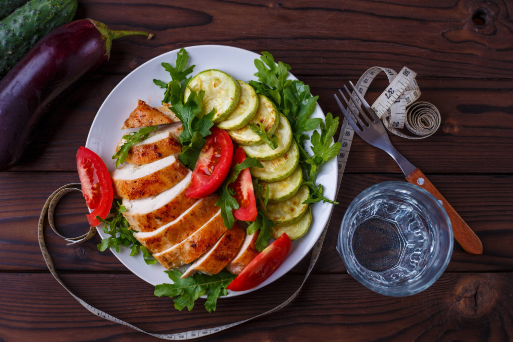 Diet concept, healthy lifestyle, low calorie food. Baked chicken breasts with zucchini and salad, measuring tape, glass of water and vegetables on the table