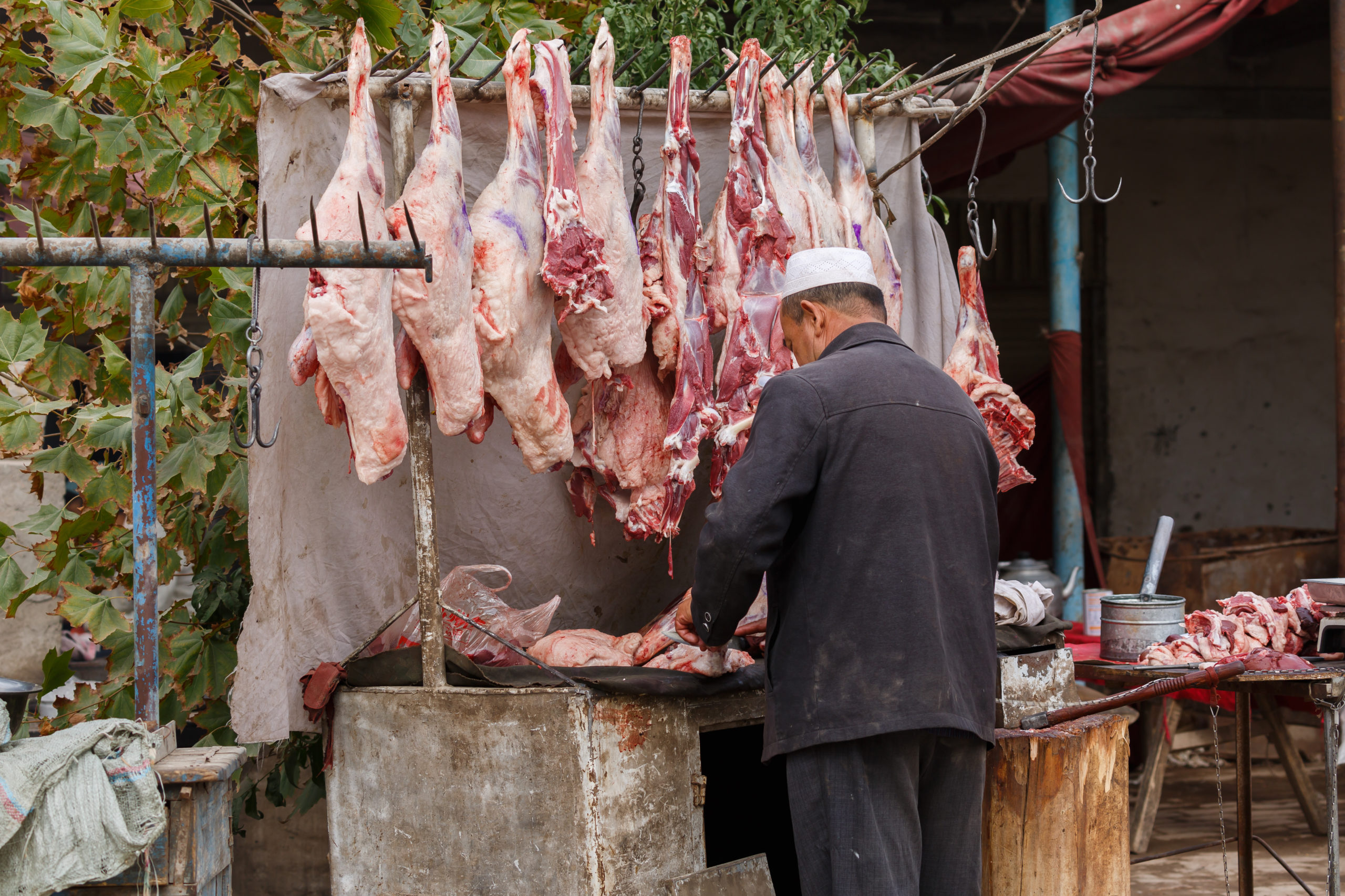 Venditore di carne in un mercato locale, banco con pezzi di carne appesi all'aperto; concept bushmeat, wet market