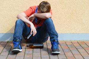 Ragazzo seduto a terra con bottiglie di birra; concept: alcol, alcolismo, dipendenza, sbornia, ubriacatura