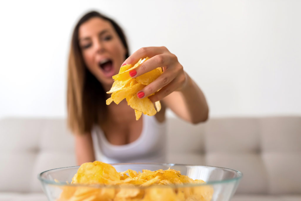 A young beautiful Woman relaxing on a sofa having potato Chips