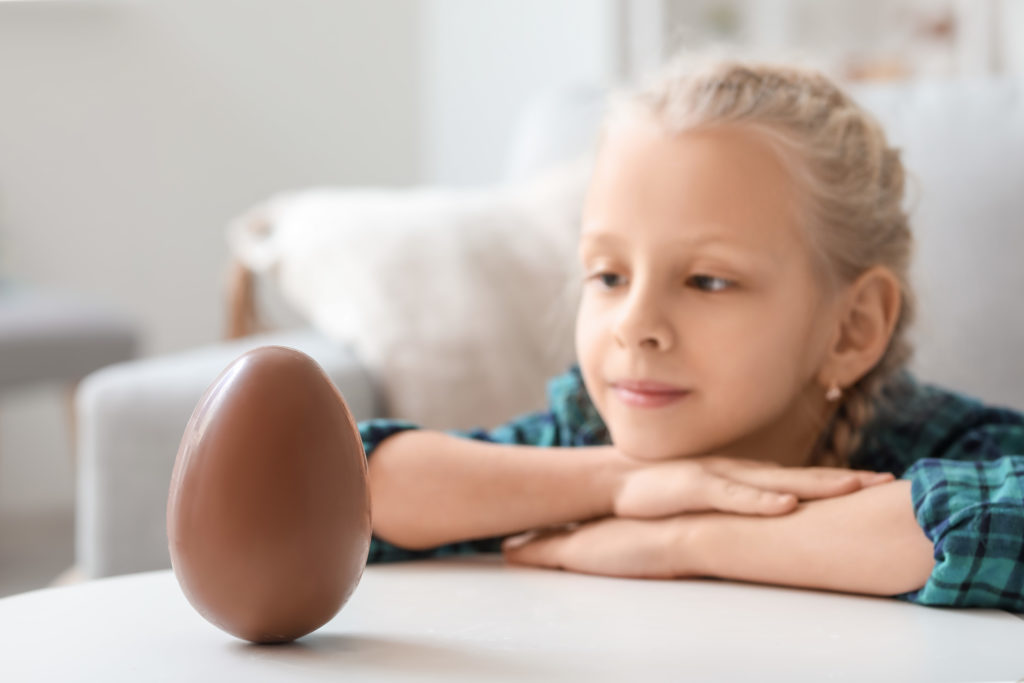 Cute little girl with sweet chocolate egg at home