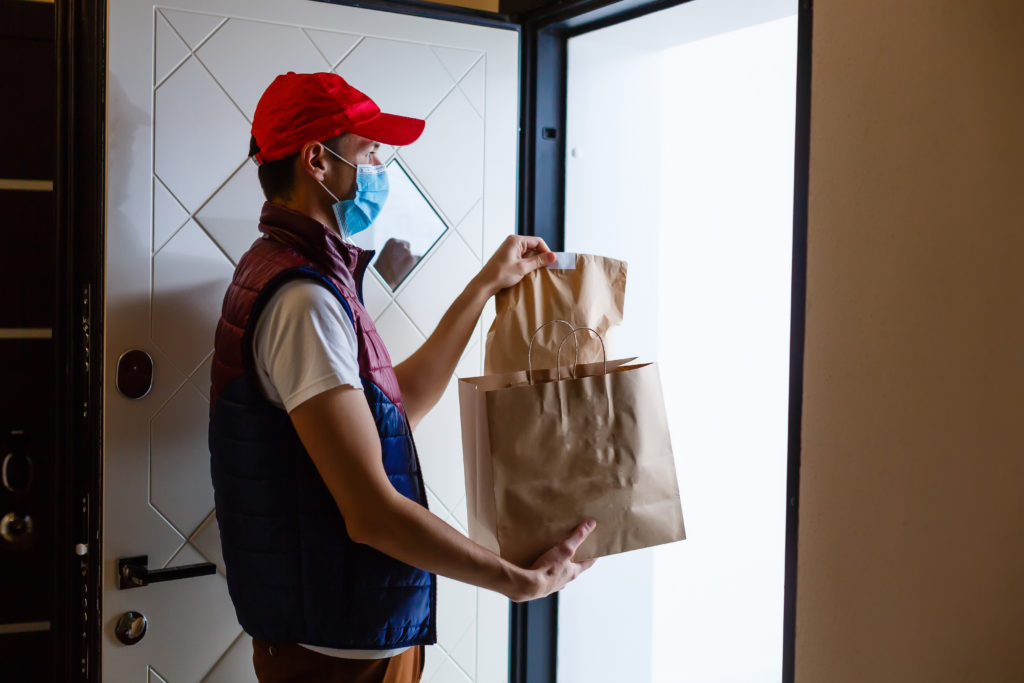 Delivery man holding paper bag with food on white background, food delivery man in protective mask