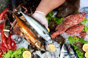 Un pescivendolo tiene in mano due pesci freschi sopra il banco della pescheria