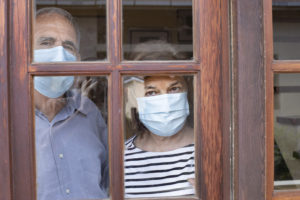 Coppia di signori anziani dietro a una finestra con mascherine; concept: covid-19, coronavirus, pandemia