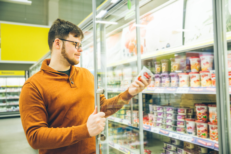 Uomo prende una confezione di yogurt dal banco frigo di un supermercato
